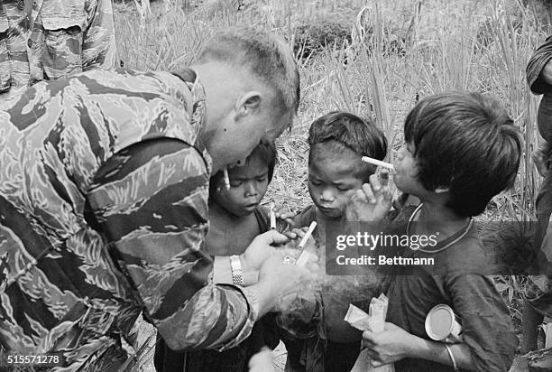 Montagnard children having a U.S. Soldier light their cigarettes. Undatd photograph.