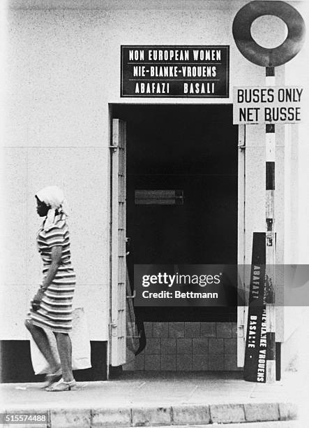 An African woman leaves a non-white toilet in Soweto, the sprawling African township on the outskirts of Johannesburg. Bold letters in English,...