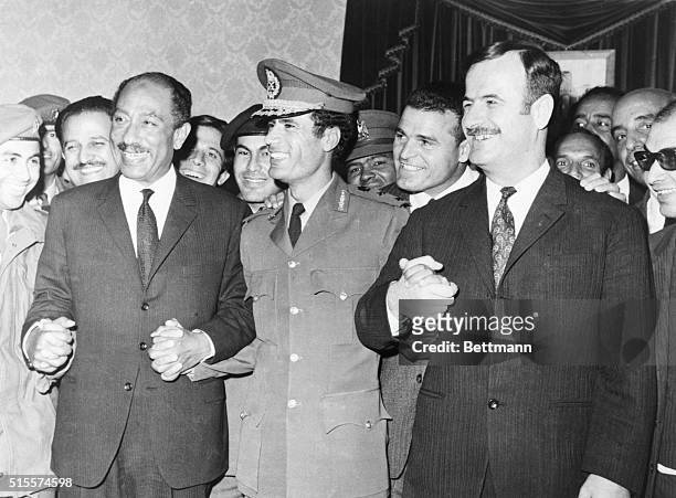 All smiles, Pres. Anwar Sadat of Egypt, Premier Col. Moammar Khadafy of Libya, and Pres. Lt. Gen. Hafez Assad of Syria, join hands after signing...