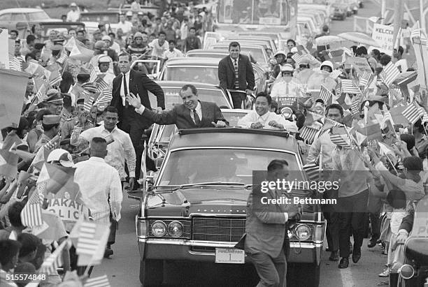 Surrounded by flag-waving crowd, Pres. Richard Nixon and Philippines Pres. Ferdinand E. Marcos wave from car during motorcade to Malacanang Palace...