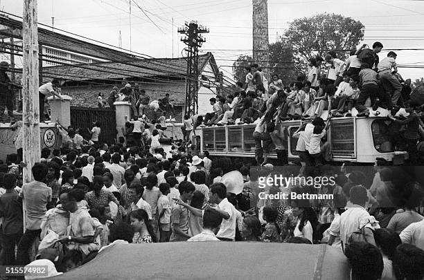 Vietnamese civilians climbing on board a U.S. Bus carrying evacuees into the U.S. Embassy, while hundreds milled around the gate, trying to get in to...