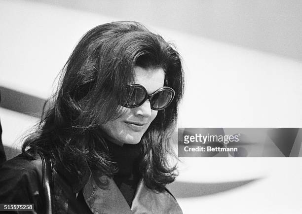 Jacqueline Kennedy Onassis, wearing dark glasses and black leather coat over a black outfit, leaves her chartered Olympic Airlines plane after...