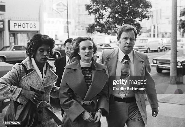 Newspaper heiress, Patty Hearst, is led to her 1976 trial by two federal marshals.