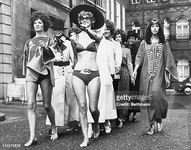 Group of fashion models march down the street donned in long dresses, maxi-coats, and chain-decorated bikinis represented in the collection shown...