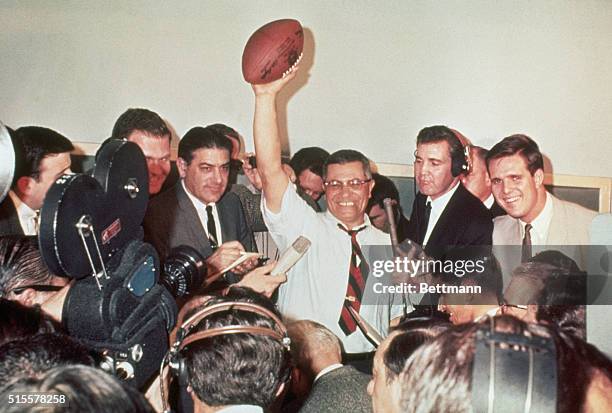 Green Bay Packers coach Vince Lombardi raises a football in victory, surrounded by reporters covering the first Super Bowl in 1967.