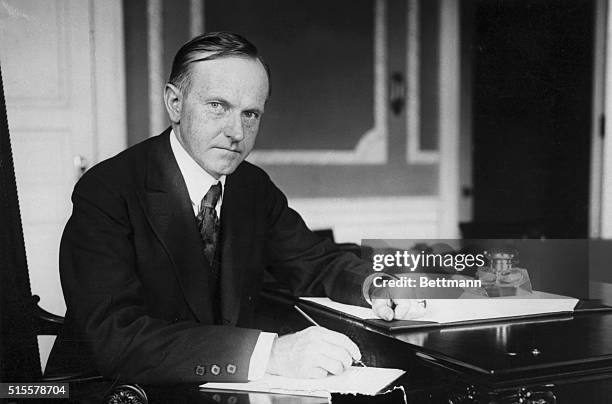 Calvin Coolidge , 30th President, sitting at his desk. Photograph.