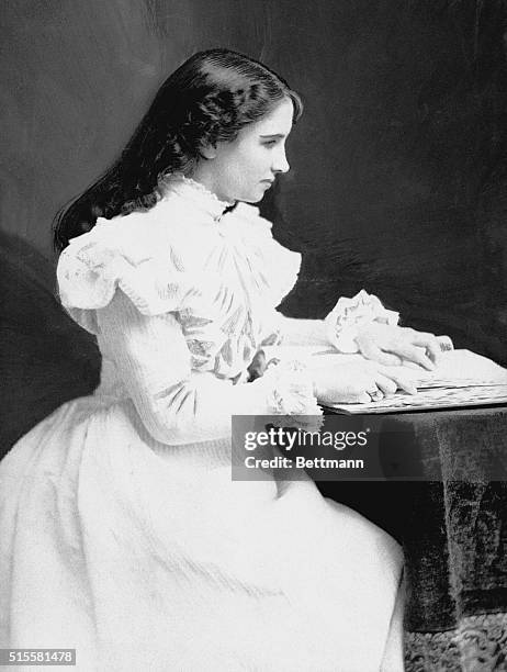 Young Helen Keller sits with a book at her desk. Due to illness, Keller suffered loss of sight and hearing at the age of 19 months.