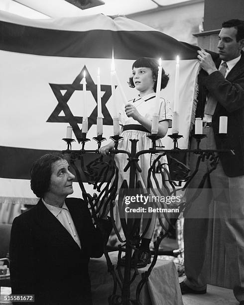 New York, NY: Mrs. Golda Meir, Israel's Chief Delegate to the United Nations, is shown with five year old Rosalyn Kramer, who is lighting five...