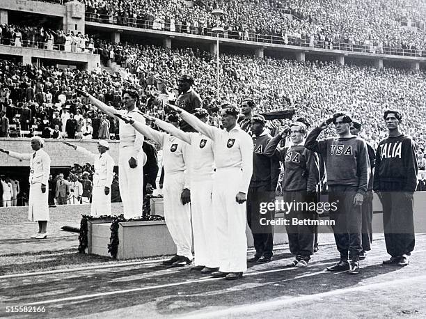 The German, American, and Italian olympic relay teams stand before the crowd at a medal ceremony. The American team composed of Ralph Metcalfe, Jesse...