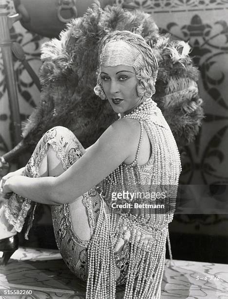 Anita Garvin models pearl beaded outfit in front of large feather fan. Undated photograph.