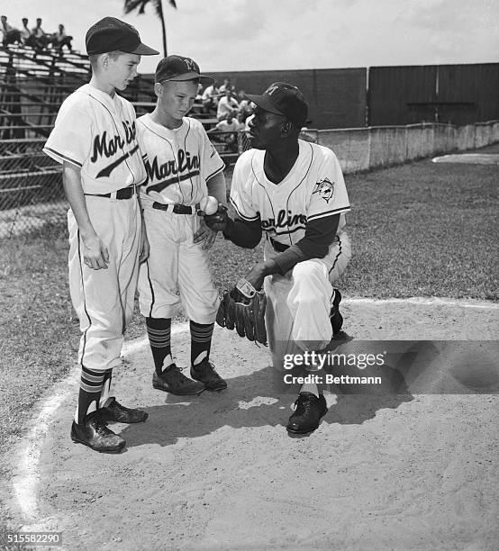 Leroy "Satchel" Paige, relief pitcher for the Miami Marlins of the International League, gives baseball pointers to two young boys dressed in...