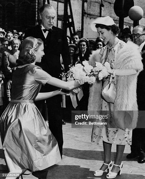 Crown Princess Elizabeth accepts a bouquet offered by Anna Massey, daughter of actor Raymond Massey, outside a London theater. The Princess was at...