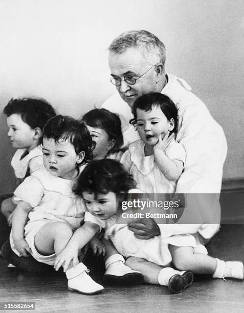 Callender, Ontario: Honored guest Dr. Allan R. Dafoe puts his arms around all five of the Dionne quintuplets -- Marie, Emelie, Cecile, Annette and...