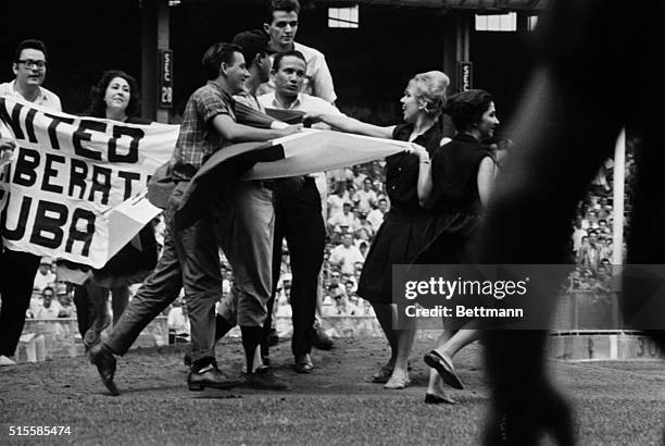 New York, NY: Anti-Castro Cubans wrap a Cuban flag and a banner calling for he liberation of Cuba around countryman Minnesota pitcher Camilio Pascual...