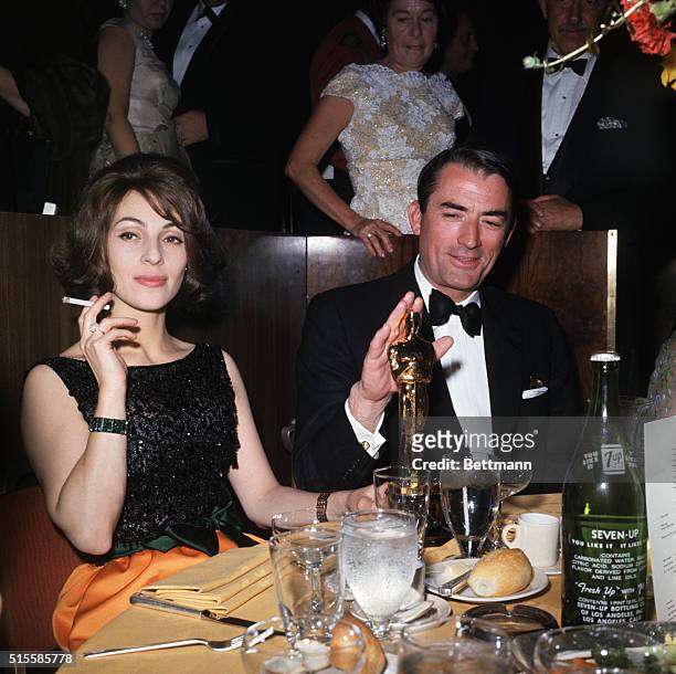 Beverly Hills, CA: Academy Awards party held at the Beverly Hilton Hotel, Berverly Hills CA. Gregory Peck and his wife seated with an Oscar.