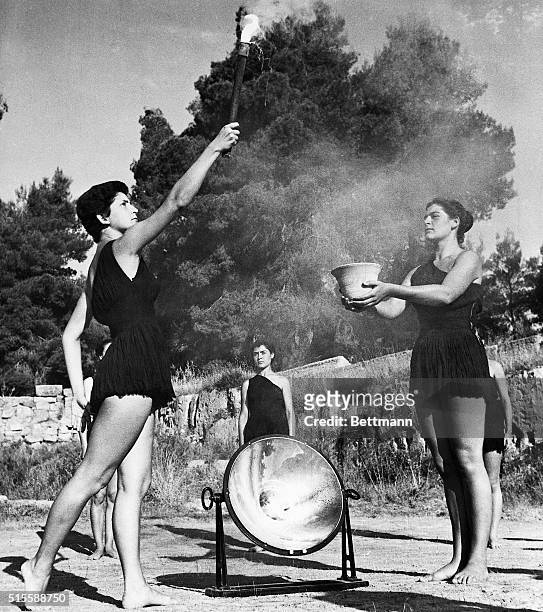 Olympia, Greece- Young Greek girls, dressed in appropriate Ancient Greek costumes, light the Olympic torch. The flame is created through the sun rays...