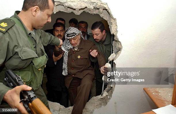 With the help of his bodyguards, Palestinian leader Yasser Arafat climbs March 16, 2002 through a hole in a wall made by Israeli troops during their...