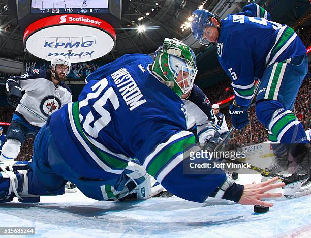 Jacob Markstrom of the Vancouver Canucks reaches back with his bare hand to make a save as Mathieu Perreault of the Winnipeg Jets and Luca Sbisa of...