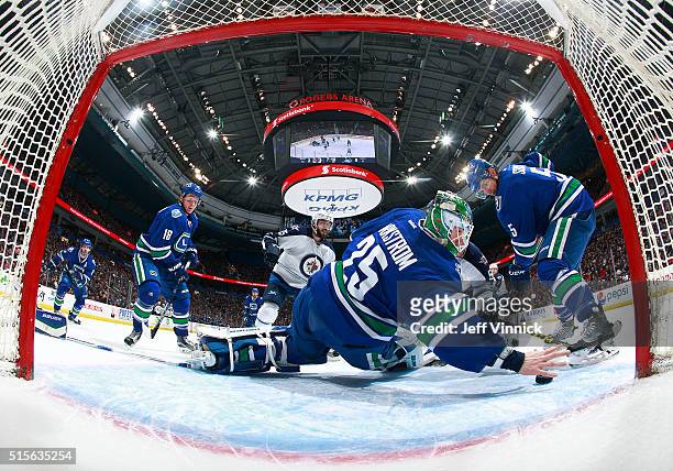 Jacob Markstrom of the Vancouver Canucks reaches back with his bare hand to make a save as Mathieu Perreault of the Winnipeg Jets, Jake Virtanen and...