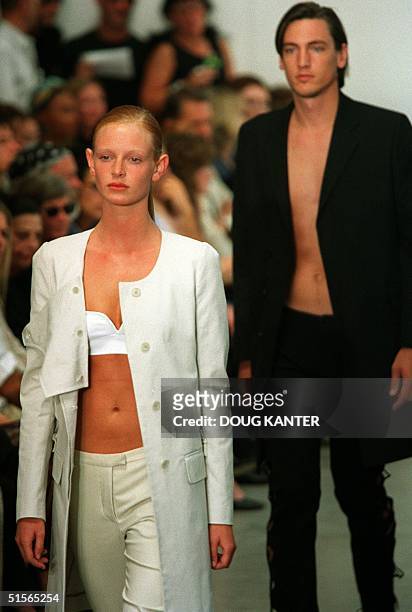 Woman model in white pants, jacket and top and a male model in a black jacket and pants make their way down the runway during the Helmut Lang show...