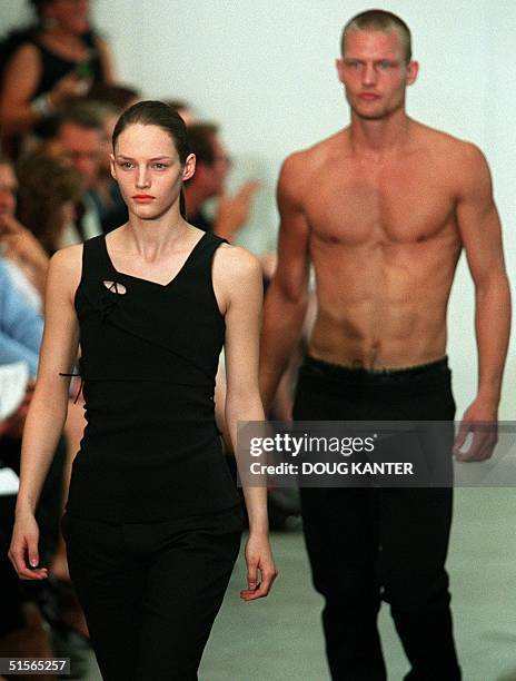 Woman model in a black top and pants and a male model in black pants make their way down the runway during the Helmut Lang show during Spring 2001...