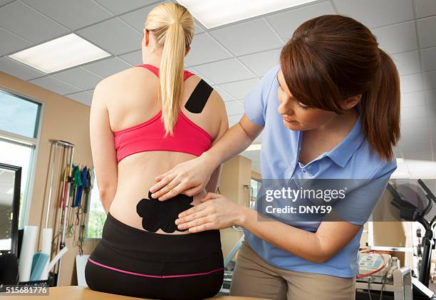 physical therapist applying kinesio tape to patient's lower back - kinesiotape stock pictures, royalty-free photos & images