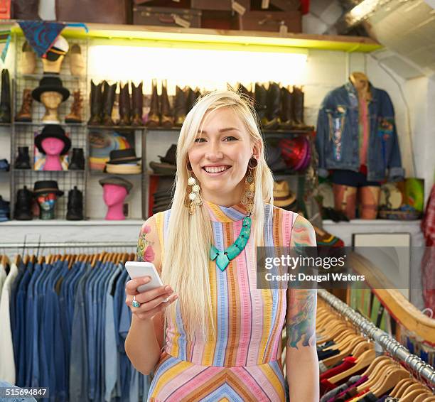 woman using mobile phone in vintage clothes shop. - multi colored dress - fotografias e filmes do acervo