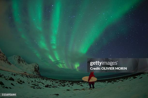 Surfer stands by northern lights on the snow covered beach of Unstad, on Lofoten Island, Arctic Circle, on March 10, 2016. Surfers from all over the...