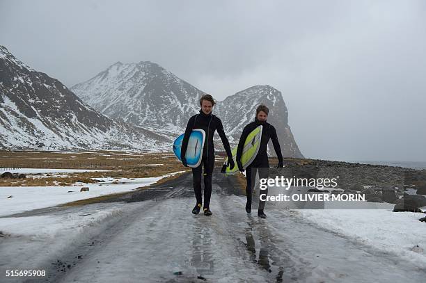 Young Swedish surfers go to the water at the end of afternoon, after spending the night under a tent at the snow covered beach Unstad in Lofoten...