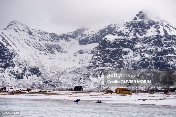 Surfers walk on the snow covered beach of Flakstad, near Rambeg, as they have a break during a surf session on the Lofoten Island, Arctic Circle, on...