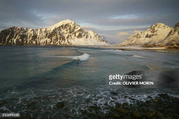 Surfers ride a wave at night time at the snowy beach of Flackstad, in Lofoten Islands, Arctic Circle, on March 12, 2016. - Surfers from all over the...