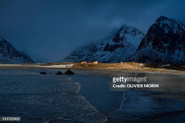 Sun ray hits the wood houses near the beach in Flakstad, near Ramberg, in Lofoten archipelago, Arctic Circle, on March 12, 2016. / AFP / OLIVIER MORIN