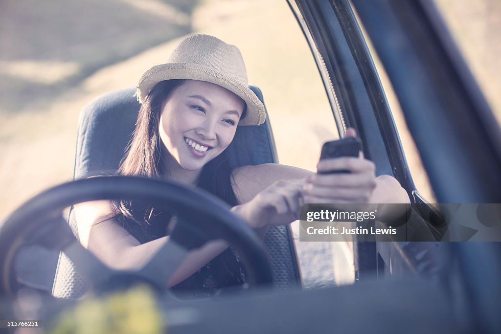 Young Asian woman in ranch truck smiling, texting