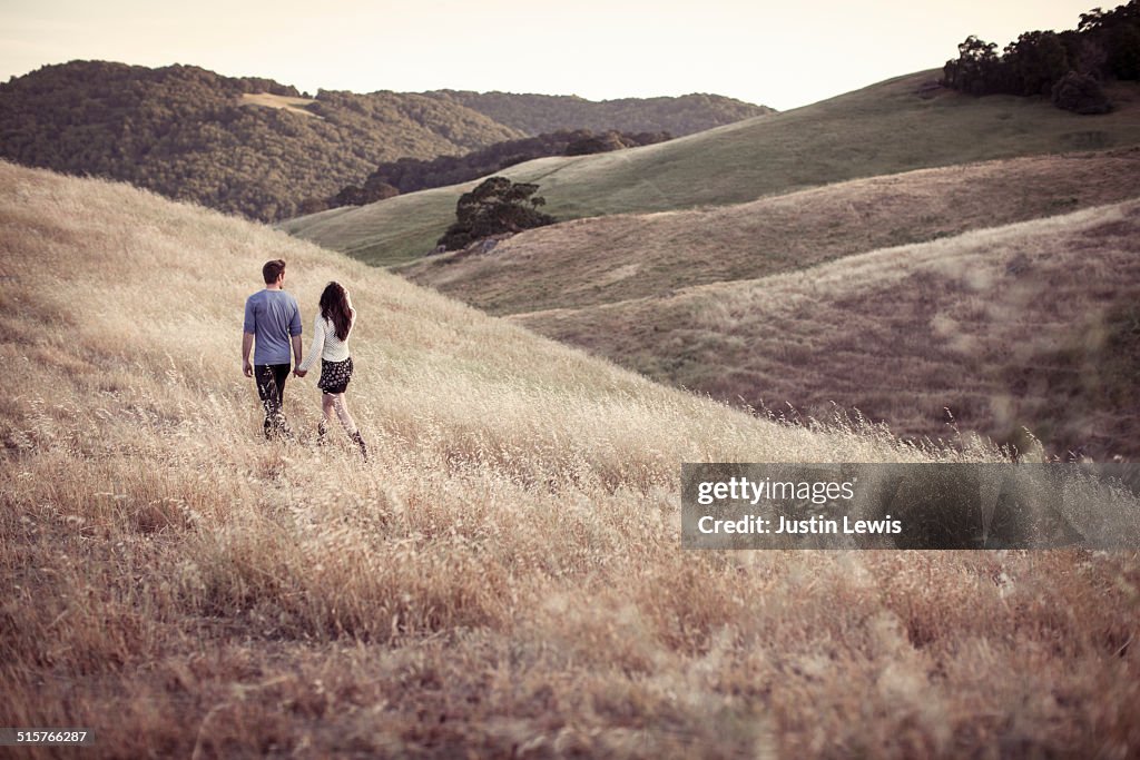 Young couple holding hands walking through fields