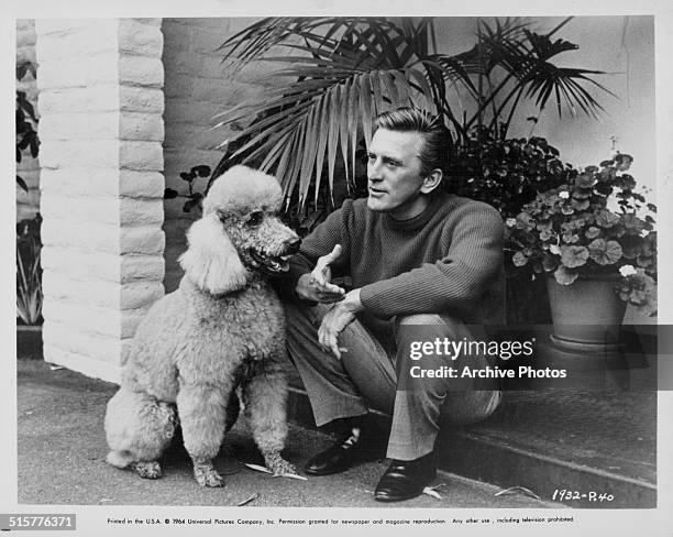 Portrait of actor Kirk Douglas and a pet poodle sitting on a step outside a house, circa 1960.