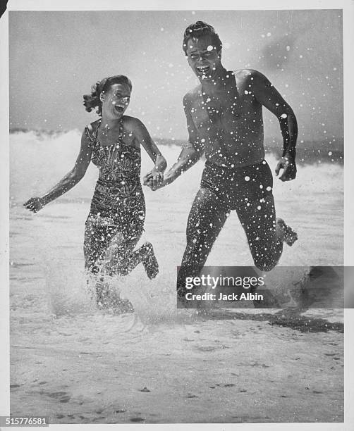 Actor John Derek and his wife Pati Behrs running through the surf on a beach, at Seafair, Laguna Beach, California, circa 1955.