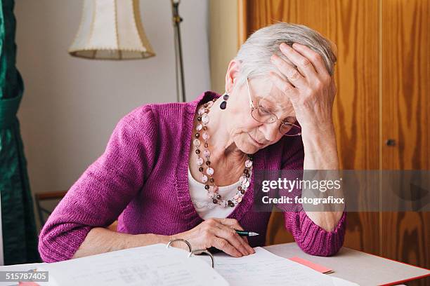 senior woman doing the paperwork in living room - bureaucracy stock pictures, royalty-free photos & images