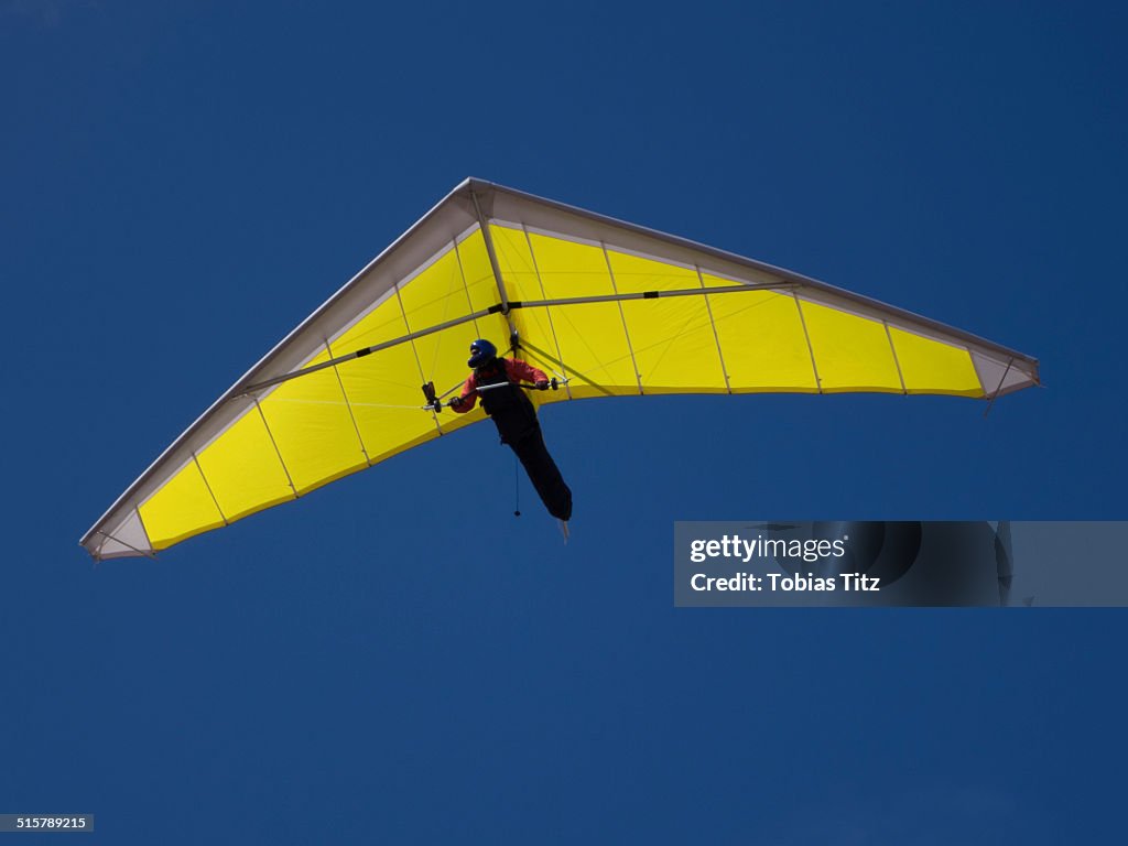 Low angle view of a person hang-gliding against clear blue sky