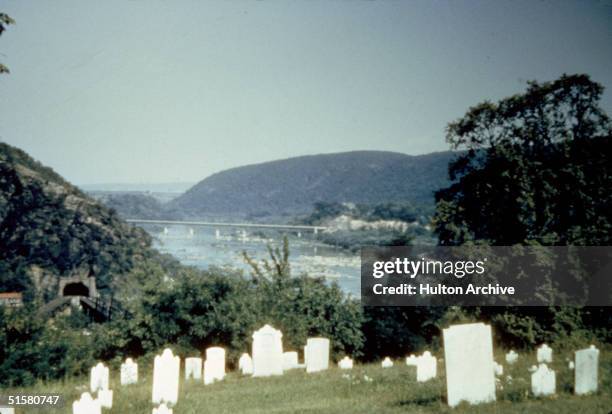 The vista across the Potomac River from Harper's Cemetery in Harper's Ferry, West Virginia, shows a railway tunnel on the left and a bridge section...