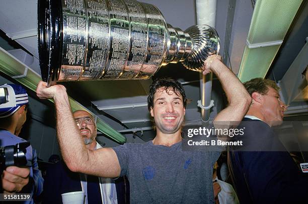 Canadian professional hockey player defenseman Paul Coffey of the Edmonton Oilers hoists the Stanley Cup over his head after the Oilers won game...