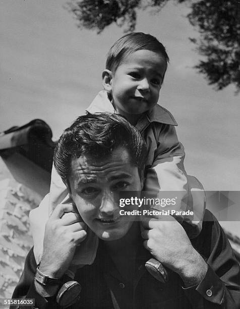 Portrait of actor John Derek, with his young son Russell on his shoulders, circa 1950.