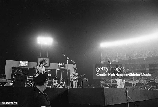Police officer in front of the stage turns to watch as the The Beatles perform at Shea Stadium, New York, August 23, 1966. L-R Paul McCartney, Ringo...