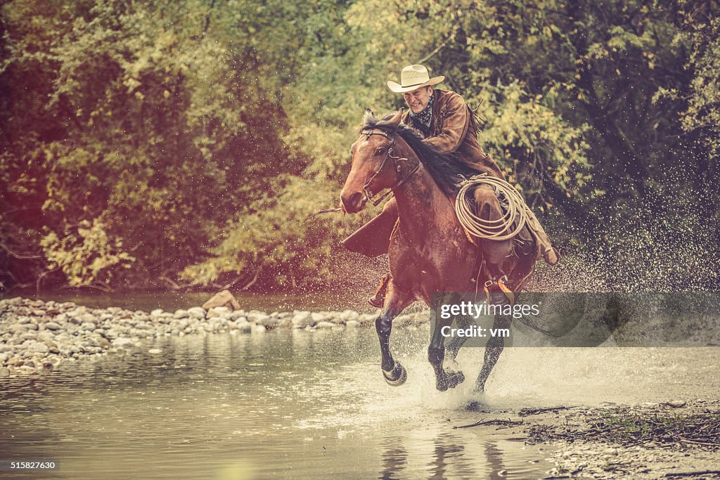 Cowboy riding across a river in the forest