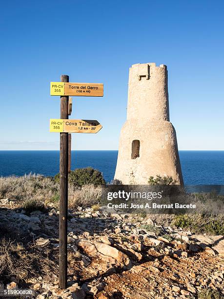 defensive tower of the 16th century on a cliff opposite to the sea and a signal with wooden arrows - denia stock pictures, royalty-free photos & images