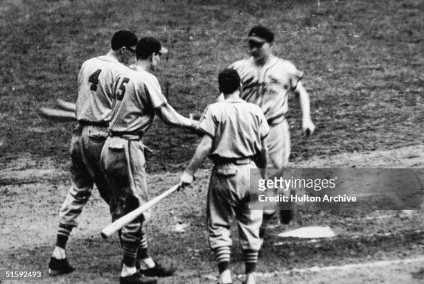 Whitey Kurowski of the St. Louis Cardinals runs across home plate after hitting a home run as his teammates Marty Marion and Walker Cooper...