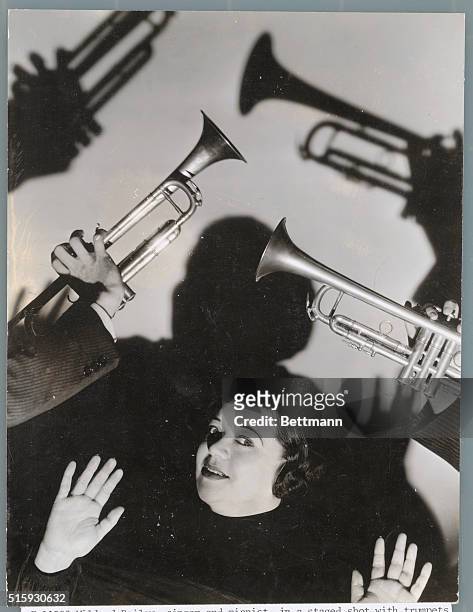 MILDRED BAILEY, SINGER AND PIANIST, IN A STAGED SHOT WITH TRUMPETS OVERHEAD AND SHADOWS ON THE WALL BEHIND. PHOTO, UNDATED.