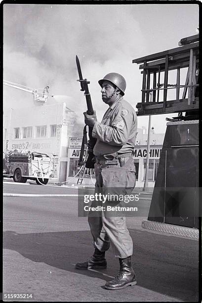 Member of the California National Guard, rifle at the ready, watches for snipers as firefighters behind him battle a blaze at a second hand store,...