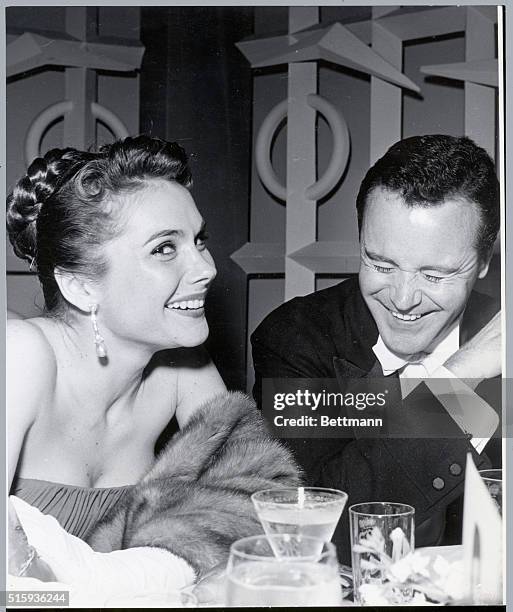 Portrait of actor, Jack Lemmon, seated next to a woman at a black tie event. They are both laughing and leaning on a table. Undated photo circa 1950s.