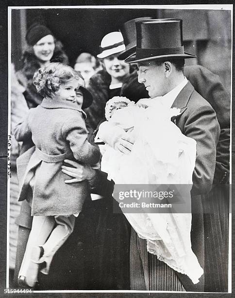 Noel Coward holds the Daniel Massey at a christening ceremony while yound Sally Pearson admires her first godson. London, December 3, 1933.