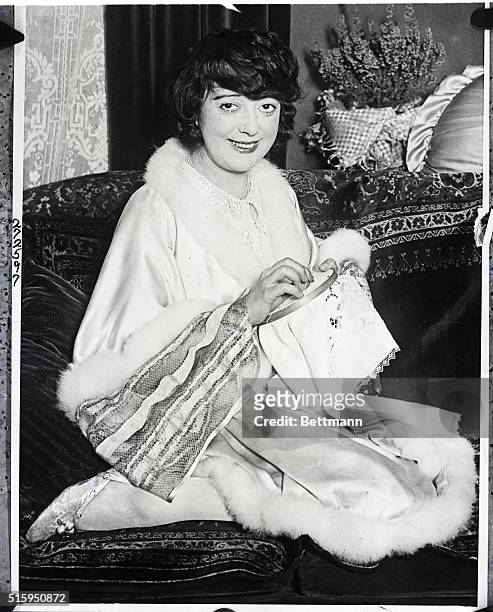 Mabel Normand smiles as she is sewing some craftwork.